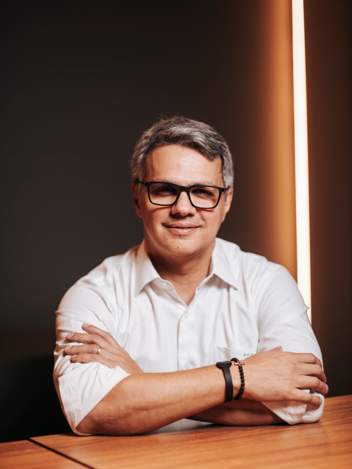 Retrato corporativo de homem de óculos com braços apoiados na mesa